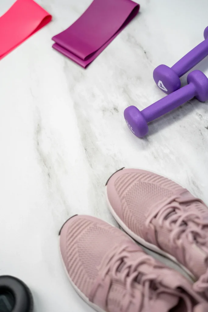 equipements-fitness-baskets-alteres-elastiques Un panel de petits équipements pour faire une séance de sport post-partum : baskets, haltères violettes, élastiques.