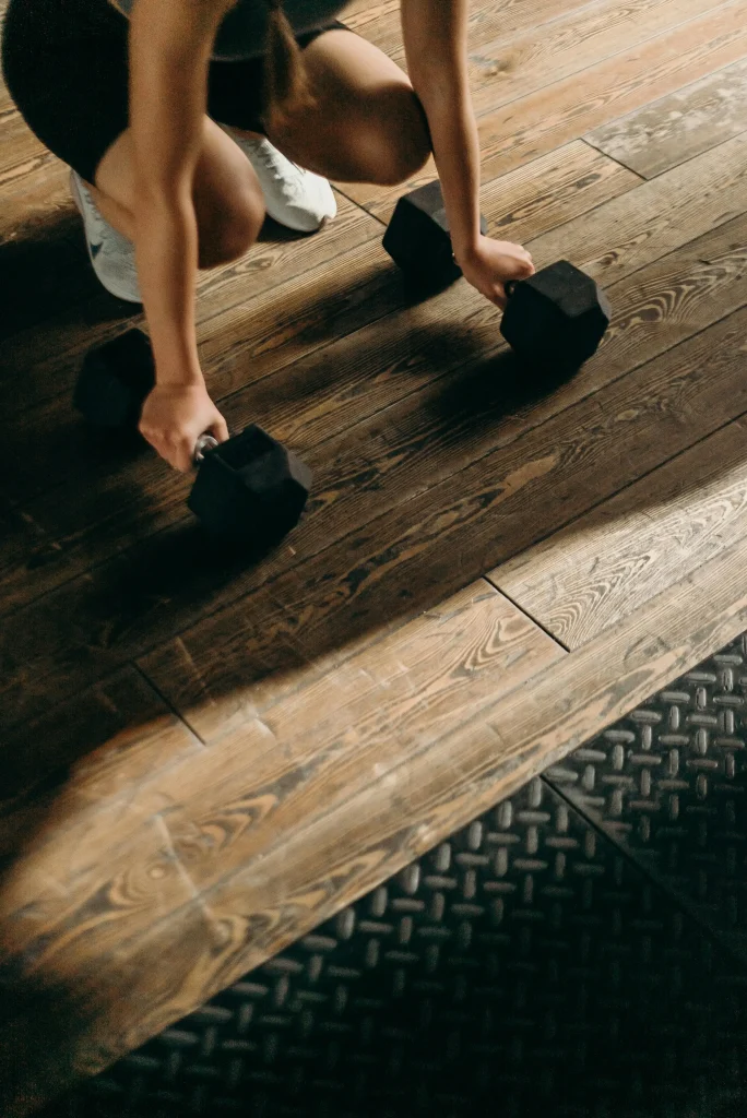 Une femme sportive est accroupie pour effectuer un exercice avec deux haltères
