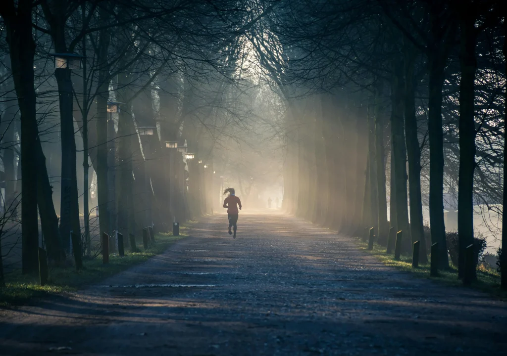 Une joggeuse coure dans un parc, sur un chemin au milieu de deux alignements d'arbres