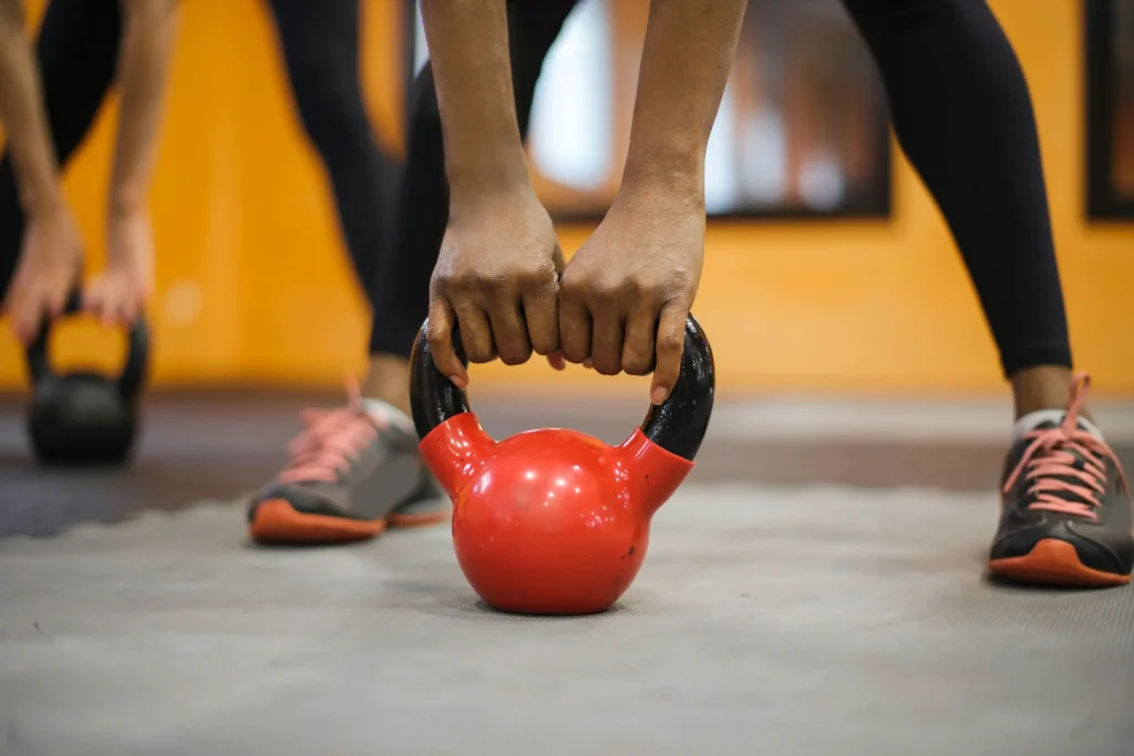 Exercice de PPG : Une femme s'apprête à soulever un kettlebell rouge du sol
