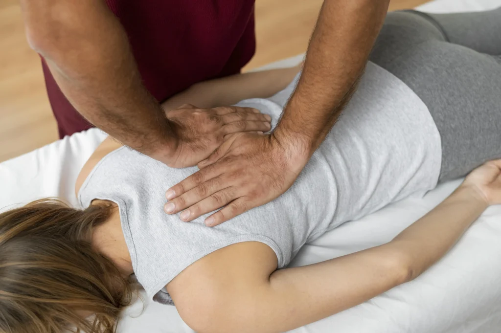 Un ostéopathe réalise une manipulation structurelle (ostéopathie) au niveau du haut du dos d'une patiente allongée.