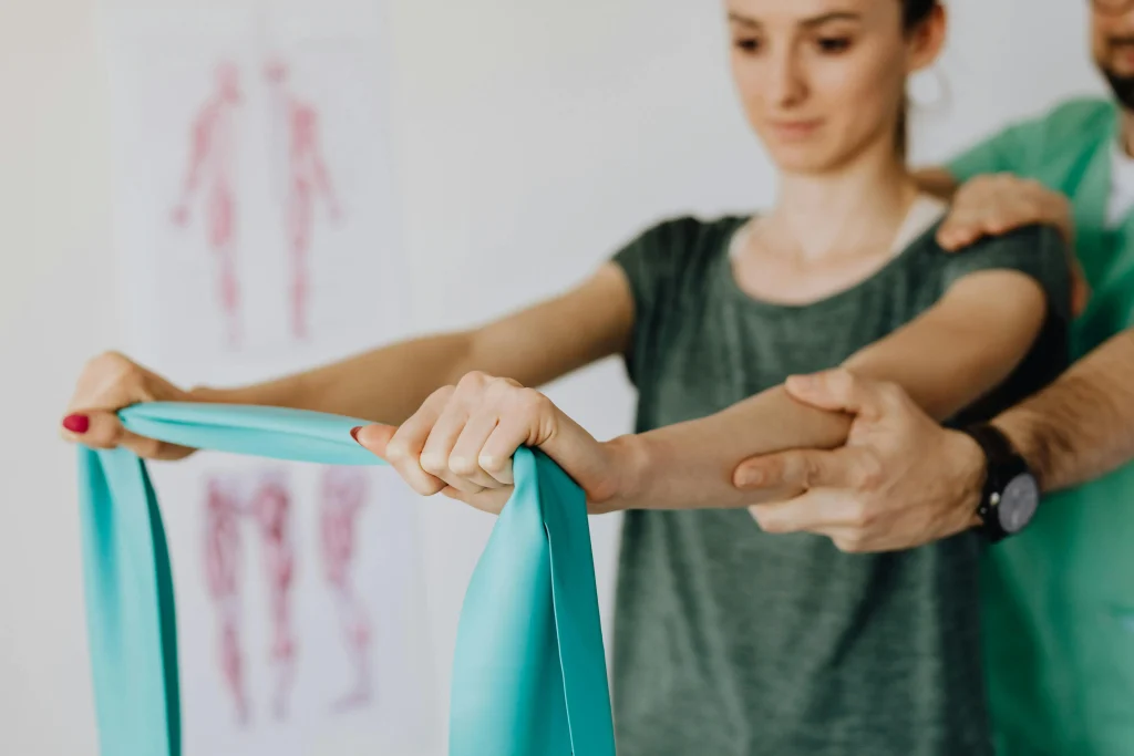 Une femme effectue des exercices avec un élastique pour son épaule. Elle est assistée par son kinésithérapeute