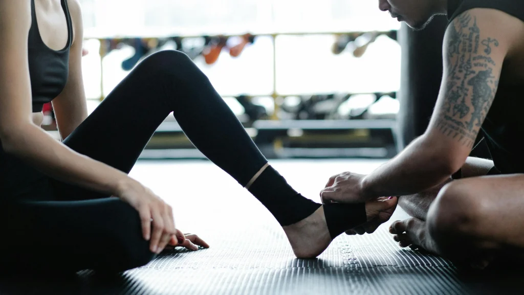soignant-patient-strap-pied Un soignant pose un strap sur le pied d'une jeune femme en tenue de sport