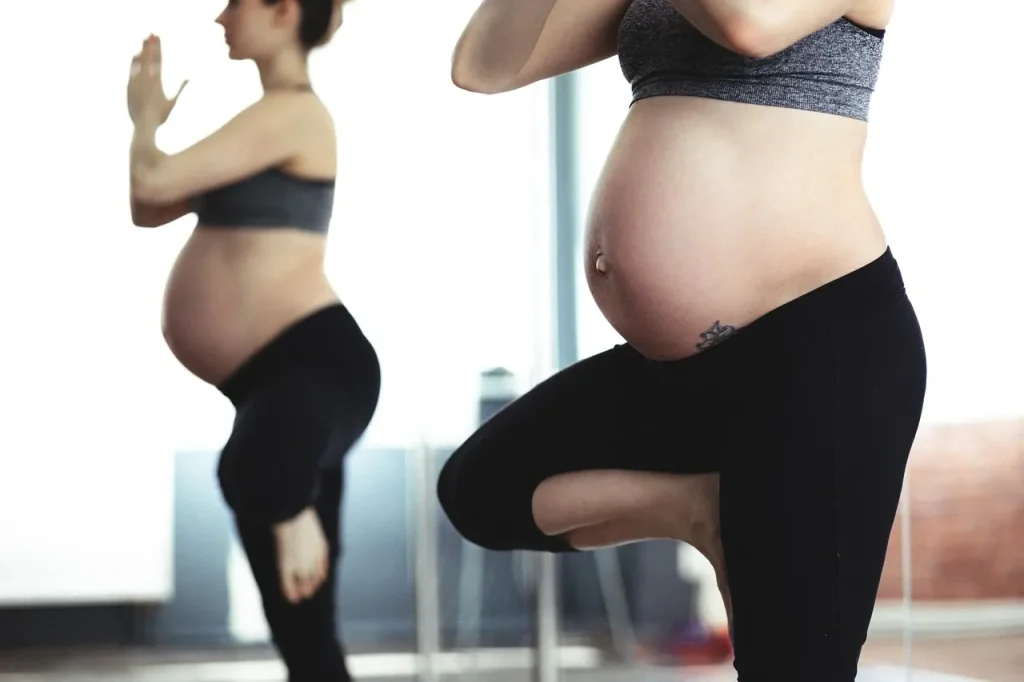 Une femme enceint est debout sur une jambe. Son reflet dans un miroir est visible.