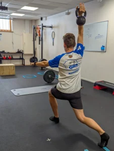Un homme réalise un exercice de fente, tenant un kettlebell dans sa main droite, sur le plateau technique du cabinet.